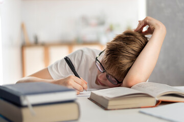 Boy is tired while doing his homework. Home schooling. Child fell asleep while studying.