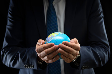 Businessman holding a globe in his hands on a dark background