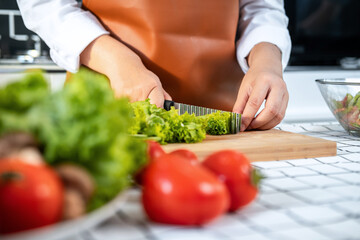 Close up of asian housewife using knife to slice lettuce on wooden chopping board to preparing ingredients