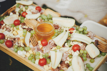 Antipasto. Cheese board with maasdam, bree, cheddar, prosciutto, salami, honey, grapes, pears and cherry tomatoes on wood. Charcuterie board. Italian appetizers for outdoor gathering party