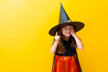 Portrait of a funny cute girl in a witch costume for Halloween. Yellow colored background, space for text.