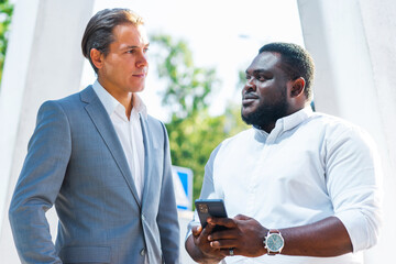 African-American businessman and his colleague in front of modern office building. Financial investors are talking outdoor. Banking and business concept.