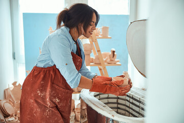 Charming female potter using electric pottery kiln in workshop