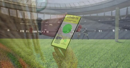 Animation of woman holding smartphone with covid 19 vaccination passport over football players
