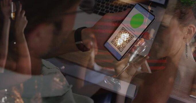 Animation of man holding smartphone with covid 19 vaccination passport over people having fun