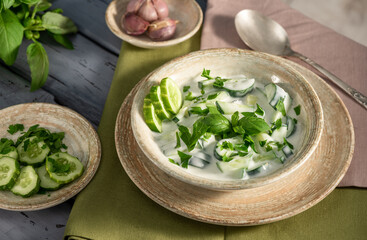 Indian spicy raita sauce with herbs and cucumbers close-up in a bowl on the table.