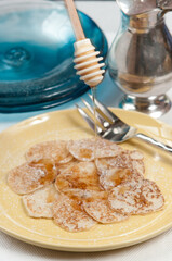 front view, close up of a pile of freshly baked, Johnny cakes, with a topping of maple syrup drizzled  on the johnnies, on a round, yellow plate with an artisan fork