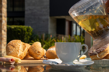 serving tea during the day in a white porcelain cup with bread and chocolate donuts in the background on a glass table