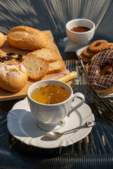 Outdoor afternoon tea, served in a white cup and spoon, with bread, jam, chocolate donuts and buttery cookies seen from above
