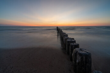 long exposure of an ocean sunset with sandy beach and wooden pylon storm groin in the foreground