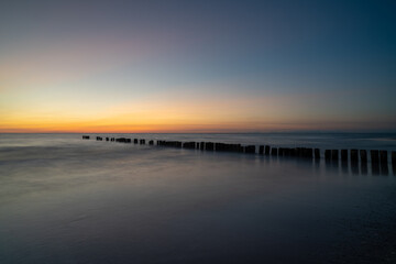 long exposure of an ocean sunset with sandy beach and wooden pylon storm groin in the foreground