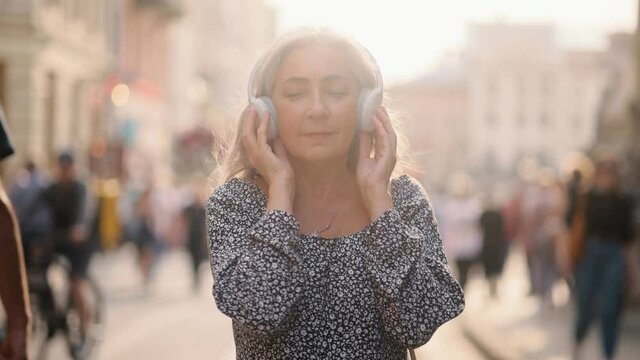 Portrait of joyful senior grey hair woman listening to music in headphones. Closeup face of beautiful middle age lady with long hair. Portrait of gorgeous woman. High quality 4k footage