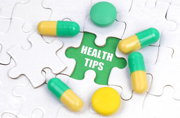 There are pills and vitamins on the white puzzles. Inside on a green background the inscription - HEALTH TIPS