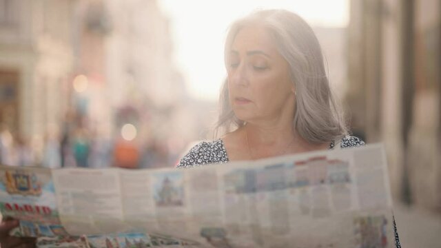 Middle aged lady walking down the street, looking for way using paper map in old town. Attractive senior tourist getting lost in big city trying to find route. . High quality 4k footage