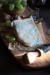 Delizioso formaggio blu con noci, uva, coltello e bicchiere di vino rosso su tagliere di legno....
