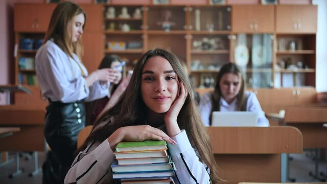 A student poses with textbooks at her desk in her class.