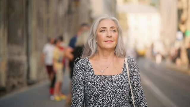Beautiful senior woman walking down the street. Attractive middle aged model standing outdoors alone. High quality 4k footage