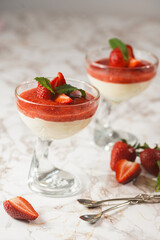 Several glasses with traditional creamy pudding dessert panna cotta with peppermint and strawberry jam surrounded fresh strawberries on a marble surface