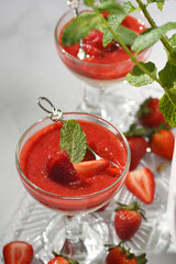 Several glasses with traditional creamy pudding dessert panna cotta with peppermint and strawberry jam surrounded fresh strawberries on a white surface