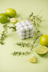 A grey bubble candle on a minty green background surrounded by limes and tree branches
