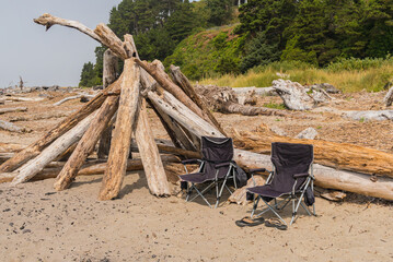 Two foldable beach chairs isolated on an ocean beach with sandals and stacked driftwood logs.