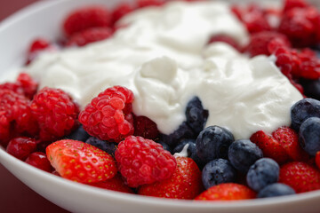 Red berry fruits and blueberries with yogurt, served in a bowl