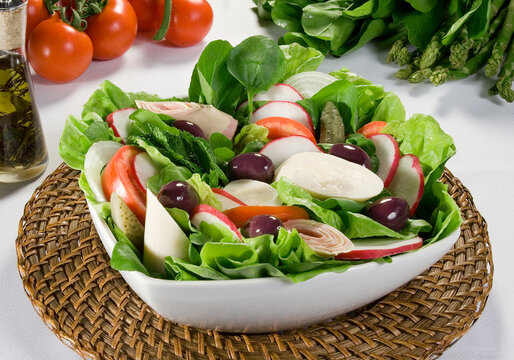 salada de folhas verdes com palmito, pepino, rabanete e azeitonas pretas, em fundo de mesa decorada.