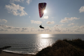 Paraglider soaring along the cliffs of Bovbjerg, Denmark during sunset.  Scenic view from top of...