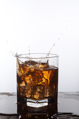 A glass filled with liquor like amber liquid splashing as ice cubes fall into it.