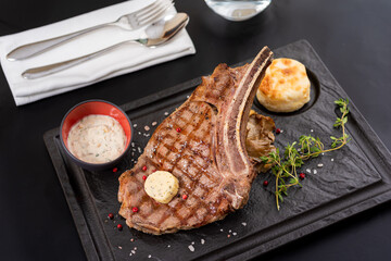 Grilled veal cutlet on black stone plate with sauce and garnish. - obrazy, fototapety, plakaty