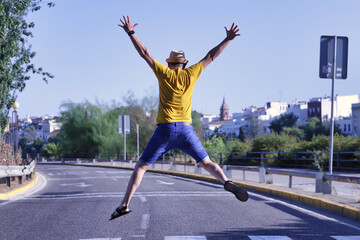 Fototapeta na wymiar Hispanic mature adult man with hat, mustard-colored t-shirt and short jeans making fun jumps over a crosswalk in the middle of the city.