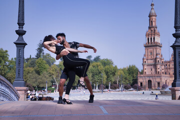 Multi-ethnic young couple doing figures while dancing bachata sensually outdoors.