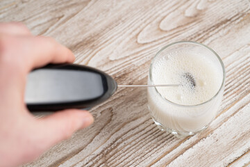 Mixing milk in glass by frother. Making foamy milk with milk frother. Milk handheld mixer.
