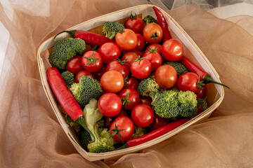 Wooden basket filled with bulk cherry tomatoes, green broccoli sprigs, and red hot chili peppers
