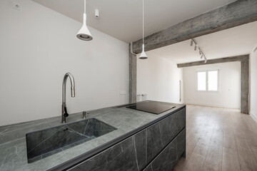 Kitchen island with sink and ceramic hob in kitchen with exposed concrete pillars and beams in a...