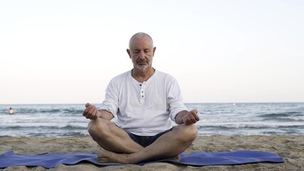 Hispanic senior man doing yoga meditation outdoor at the beach - Elderly mindfulness healthy lifestyle