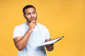 Cooking, culinary and people concept - african american indian male chef with clipboard isolated over yellow background.