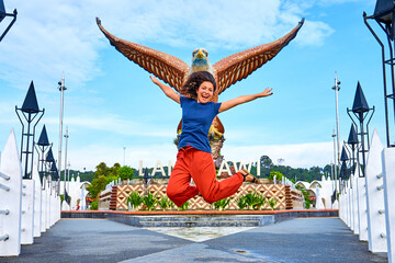 Happy girl tourist posing next to sculpture of a red eagle spreading its wings. Popular tourist...