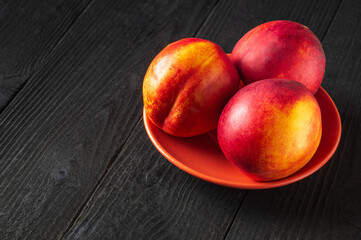 Three red ripe nectarine hybrids in their ripening season lie on orange plate or on a dark vintage table.