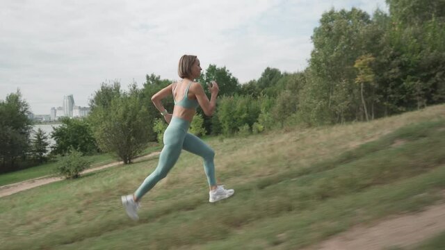 Slow motion shot young woman running on the hard trail. Young fit woman doing cardio exercise. Concept of moving forward. Long shot.