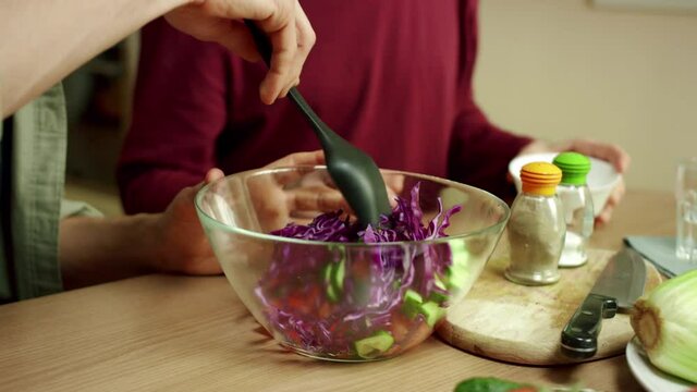 Two men are pouring the sauce over the salad and sterring it