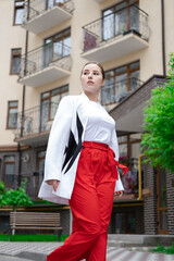 confident brunette woman in red pants and white blouse and jacket walking in the street