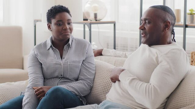 Afro american family married couple black woman and man father and daughter wife and husband sitting at home on sofa talking communication conversation talk mature male share ideas speaking explaining