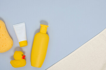 Baby care concept. Evening baby bathing. Flat lay composition of bathing accessories for newborn - towel, sponge, rubber duck, cream, shower gel - on grey background. Place for text.