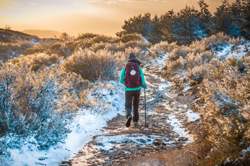Obraz premium Girl Pilgrim Hiker on the Snow Winter Mountain Forest Evening on the Way of St James Pilgrimage Trail Camino de Santiago outside El Acebo at Sunset
