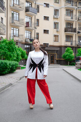 confident brunette woman in red pants and white blouse and jacket walking in the street