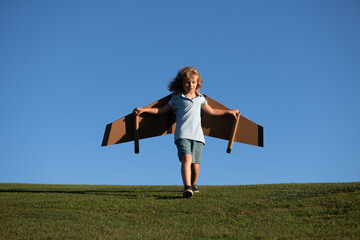 Child flying in plane made craft of cardboard wings. Dream, imagination, childhood. Travel and summer vacation concept. Young boy pilot against a blue sky with copy cpase.