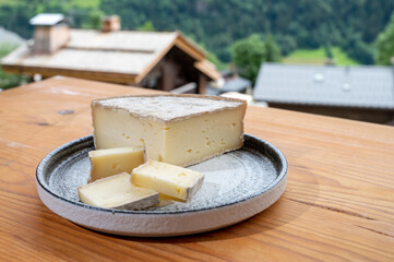 Cheese collection, French cheese tomme de savoie and french mountains village in Haute-Savoie on background - obrazy, fototapety, plakaty