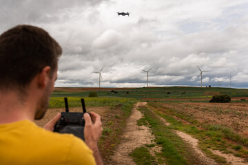 Back View Of An Unrecognizable Caucasian Young Adult Flying A Drone In A Sustainable Windmill Field. Learning Concept.