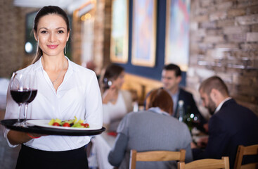Professional cheerful positive waitress holding serving tray for restaurant guests